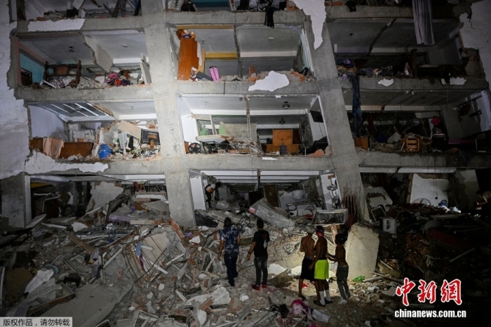 当地时间6月24日，委内瑞拉遭遇两次震级超过7级的强震，委内瑞拉宣布进入紧急状态。图为地震过后，人们站在一栋受损建筑附近的废墟前。